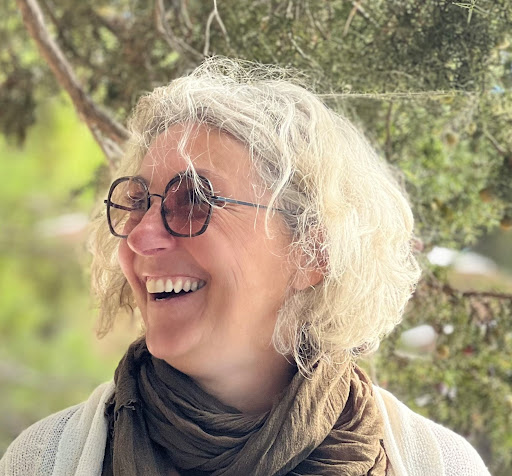 Portrait de femme souriante, lunettes, cheveux gris Femme aux cheveux gris bouclés et lunettes souriant joyeusement, un foulard terre se fond sur un arrière-plan végétal flou.