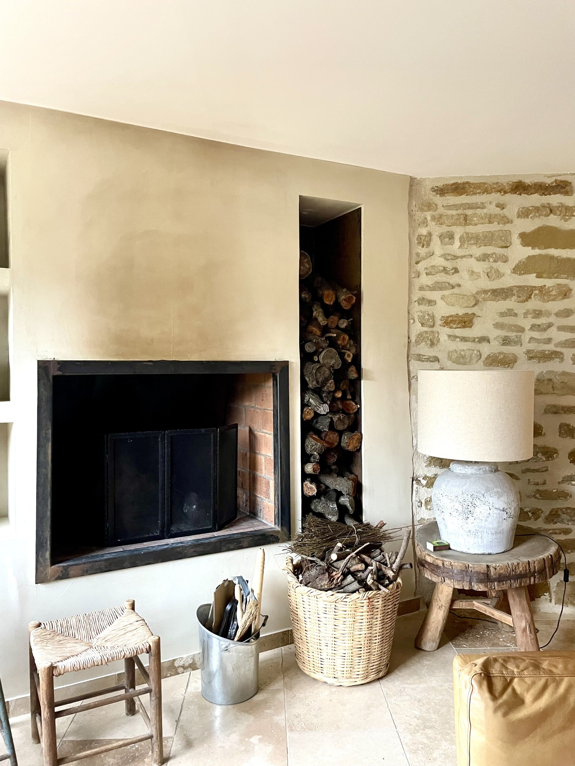 Salon rustique avec cheminée encastrée, niche à bûches verticale et mur en pierre naturelle.